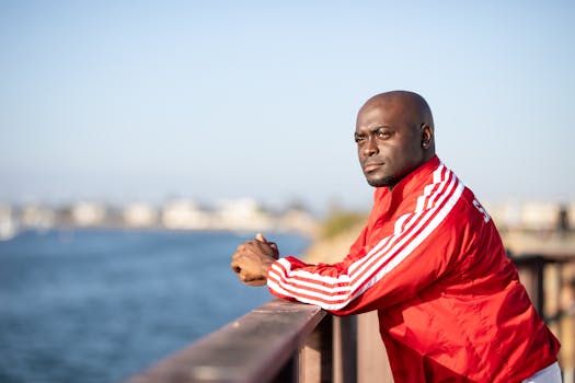 一个秃头男人穿着红色夹克，靠在栏杆上俯瞰宁静的海滨