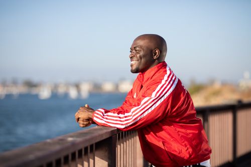 Free African American man smiling while leaning on a railing by the water. Stock Photo