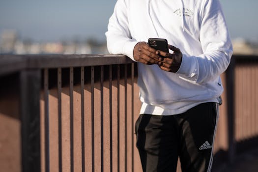 Person in white hoodie using smartphone outdoors by railing