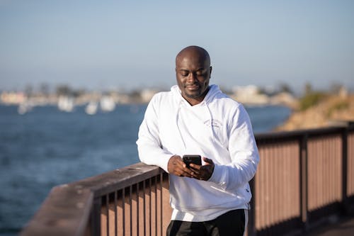 Bald Man in White Hoodie Holding a Cellphone