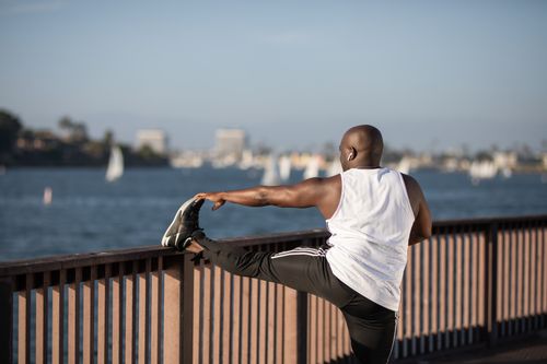 Free African American man stretching by the water, promoting outdoor fitness and healthy lifestyle. Stock Photo