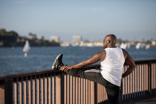 Free Bald man in activewear stretching against railing near water under clear sky. Stock Photo