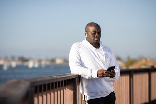 Bald Person in White Hoodie Holding a Cellphone