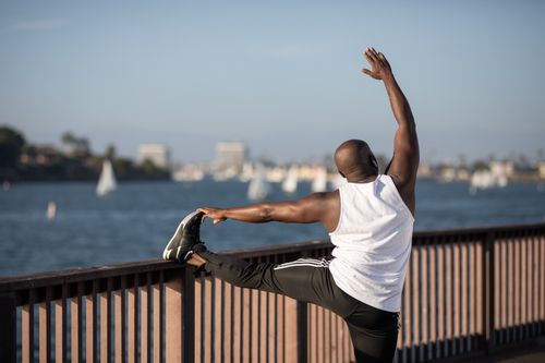 Free An adult man performs a stretching exercise by the water on a sunny day, promoting fitness and healthy living. Stock Photo