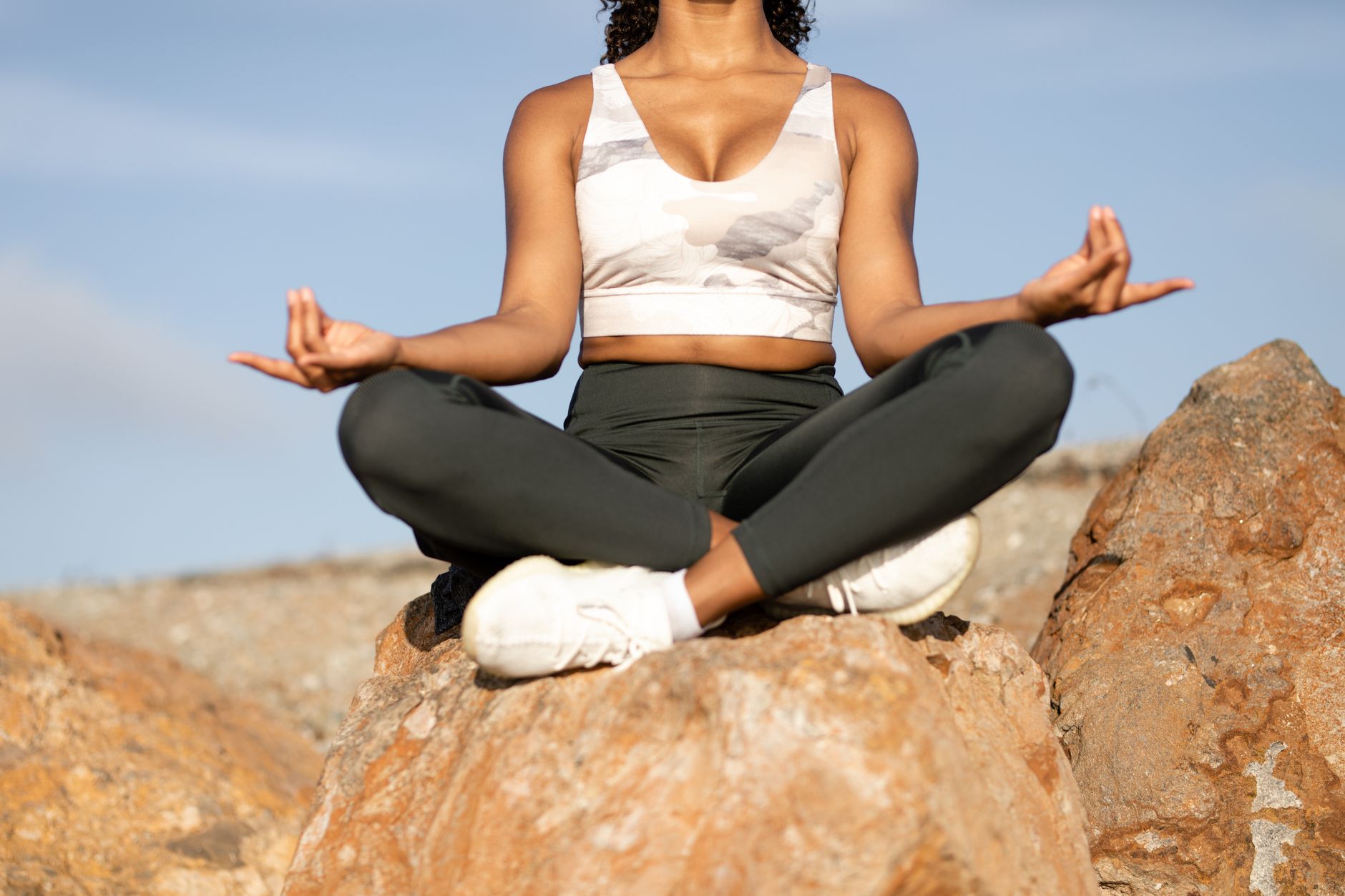 Woman meditating outdoors on rocks, promoting peace and mindfulness.