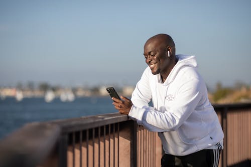 Man in White Hoodie Smiling While Holding a Cellphone