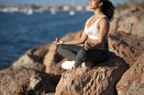 Woman Wearing Activewear Sitting on Rock While Doing Yoga