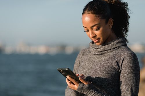 Free Young woman in a sweater looking at her smartphone by the water. Stock Photo