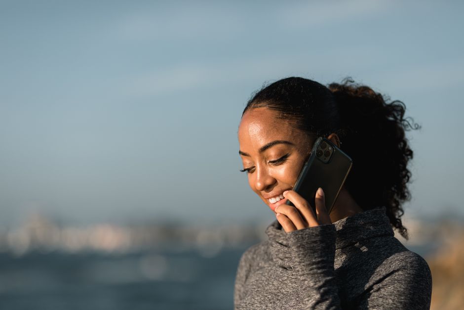 Smiling woman talking on smartphone in a sunny outdoor setting, exuding cheerful vibe.