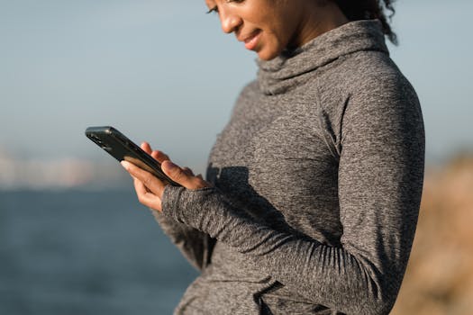 Woman in gray sweater using a smartphone outdoors by the water.