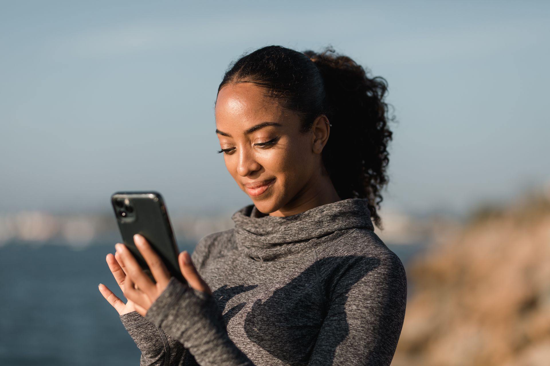 Woman in Gray Sweater Holding Black Mobile Phone