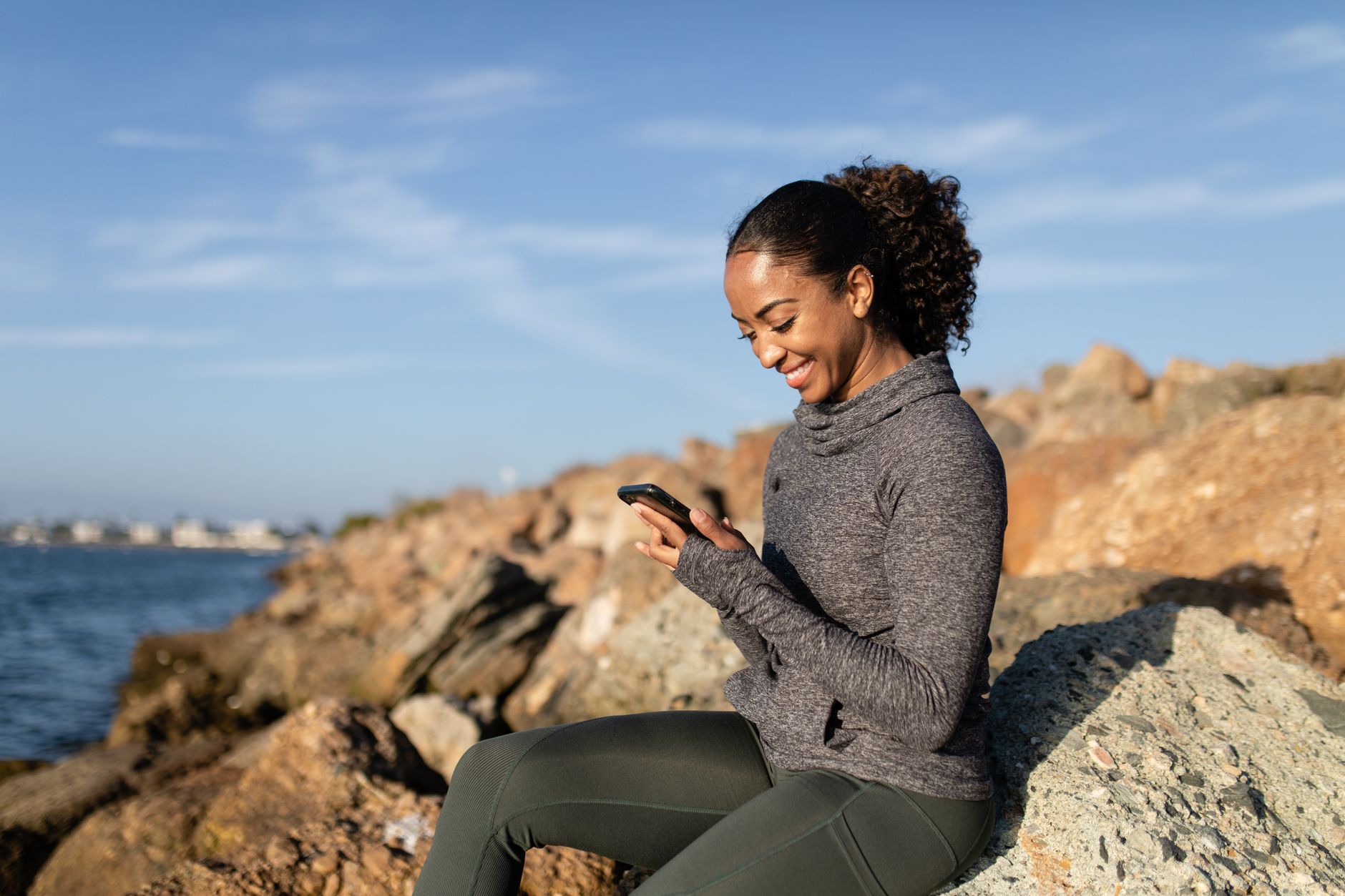 https://www.pexels.com/photo/a-happy-woman-using-her-cellphone-while-sitting-on-a-rock-4909462/