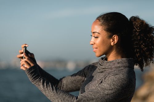 Free A young African American woman taking a selfie outdoors by the water on a sunny day. Stock Photo