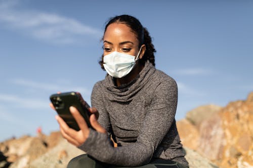 Free A Woman in a Face Mask Using her Smartphone Stock Photo