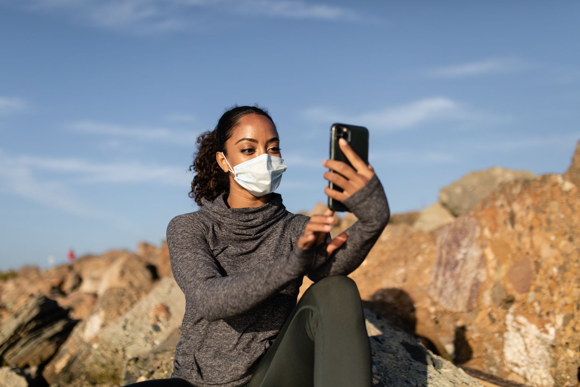 手機旅遊短影片15秒腳本庫:10組實用範例 Woman in a face mask takes a selfie in a rocky outdoor setting, capturing a sunny day moment.