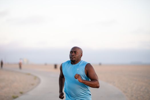 A man jogging on a sandy beach during sunset, enjoying outdoor exercise.