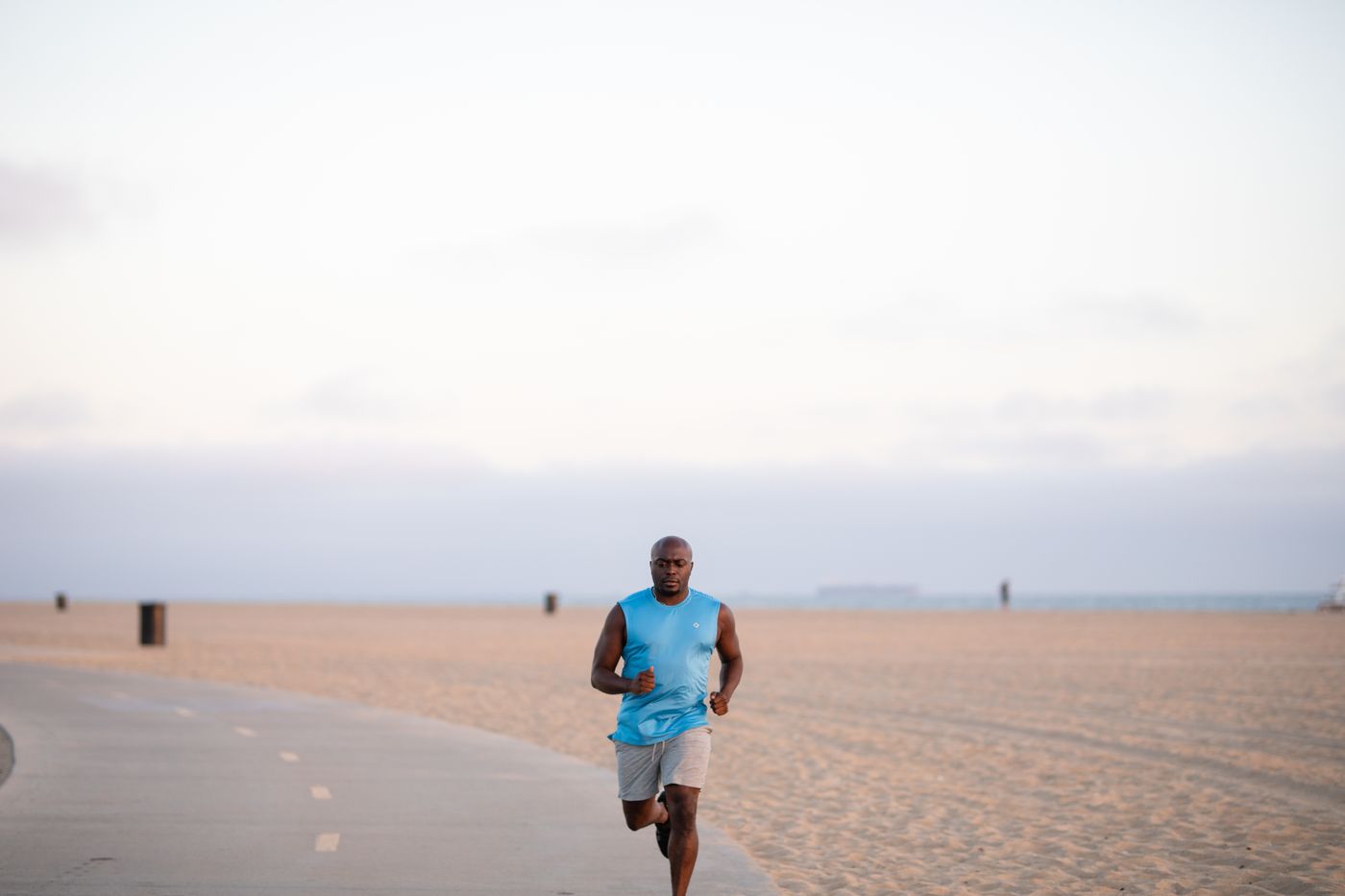 Black man running on a tree-lined coastal path in morning light