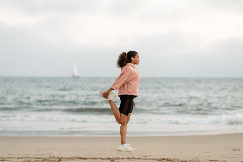 Free Woman in Pink Sweater and Black Shorts Standing on Beach Stock Photo