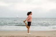 在海滩上做瑜伽时，一位身着运动服伸展的女人的侧视图