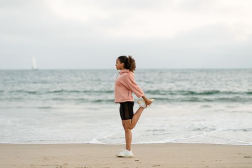 Free Side view of a woman in activewear stretching on a beach, promoting fitness and wellness. Stock Photo