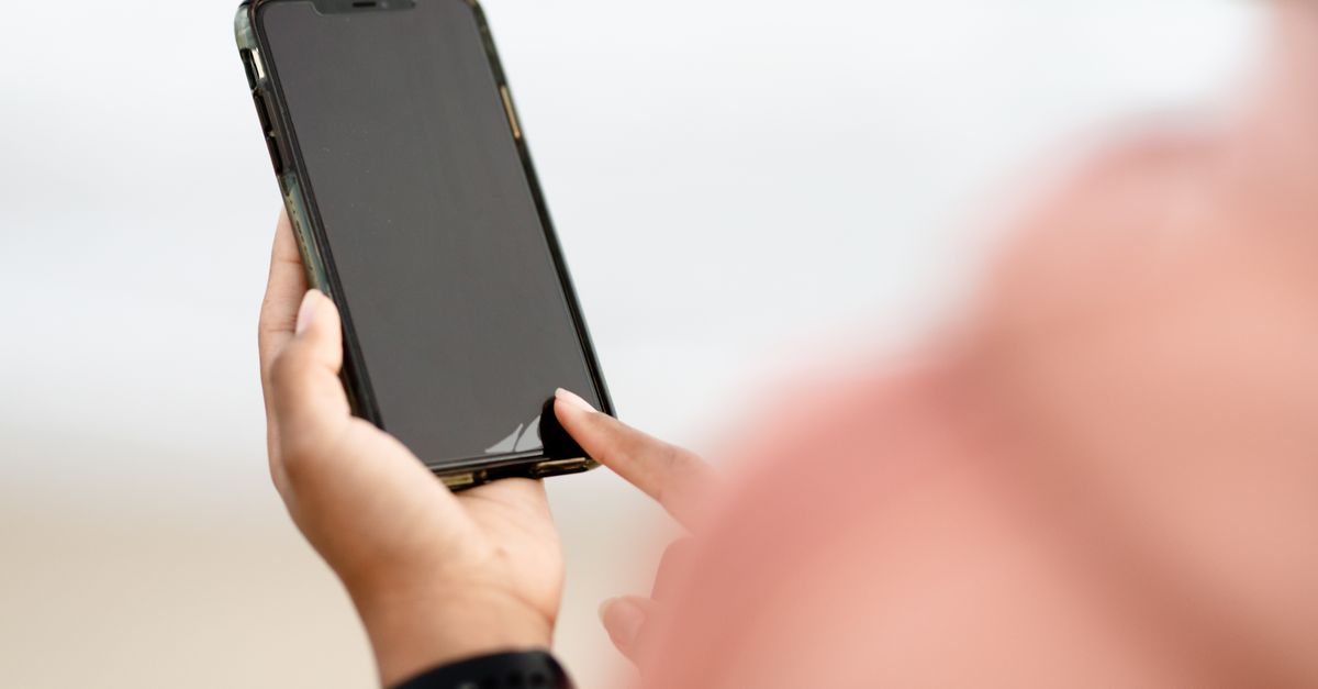 A hand interacting with a smartphone touchscreen outdoors. Modern technology concept.