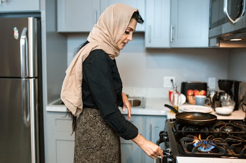 Ethnic woman in headscarf switching on stove