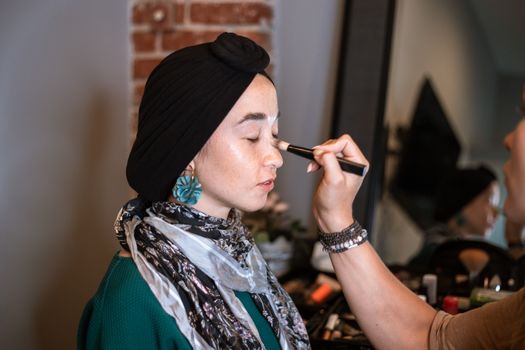 A woman wearing a hijab gets a makeover, highlighting beauty care and cosmetics indoors.