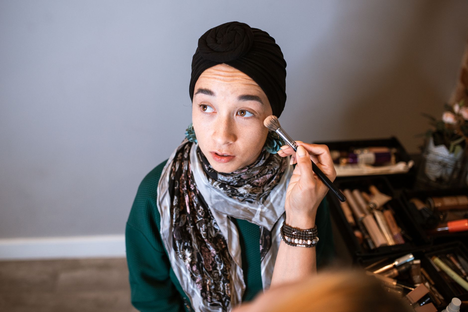 A woman in a hijab applies makeup in a well-lit indoor setting, focusing on beauty care.