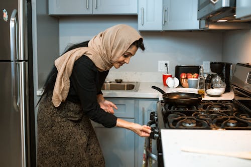 Веселая этническая женщина переключает плиту перед приготовлением пищи