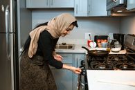 Cheerful ethnic woman switching stove before cooking