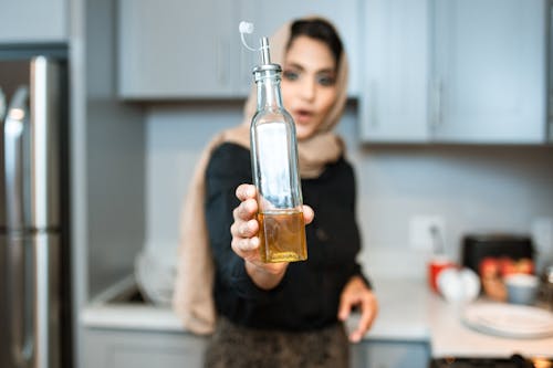 Free Ethnic woman demonstrating bottle of olive oil while cooking Stock Photo