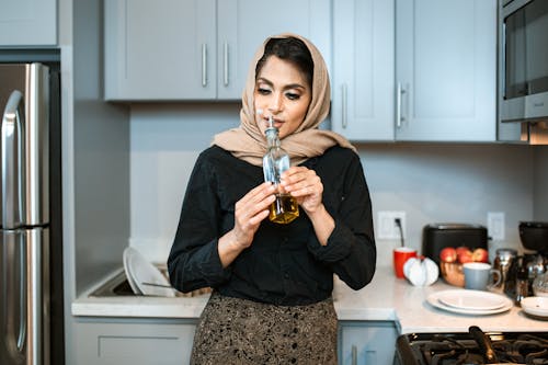 Довольная арабская женщина нюхает масло в бутылке на кухне