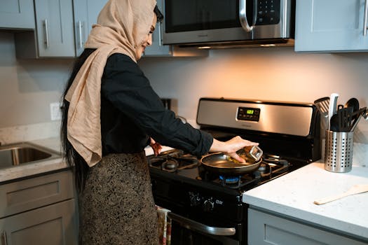 Woman in headscarf cooking in a stylish modern kitchen, pouring ingredients into a pan.