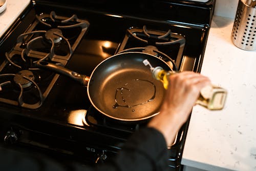 Crop unrecognizable chef pouring oil in frying pan