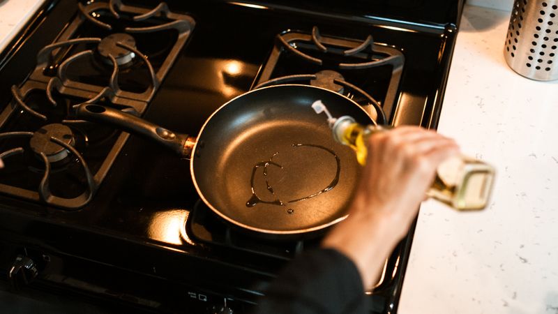 person cooking with a centered pan on a glass induction cooktop, standing a short step back from the counter