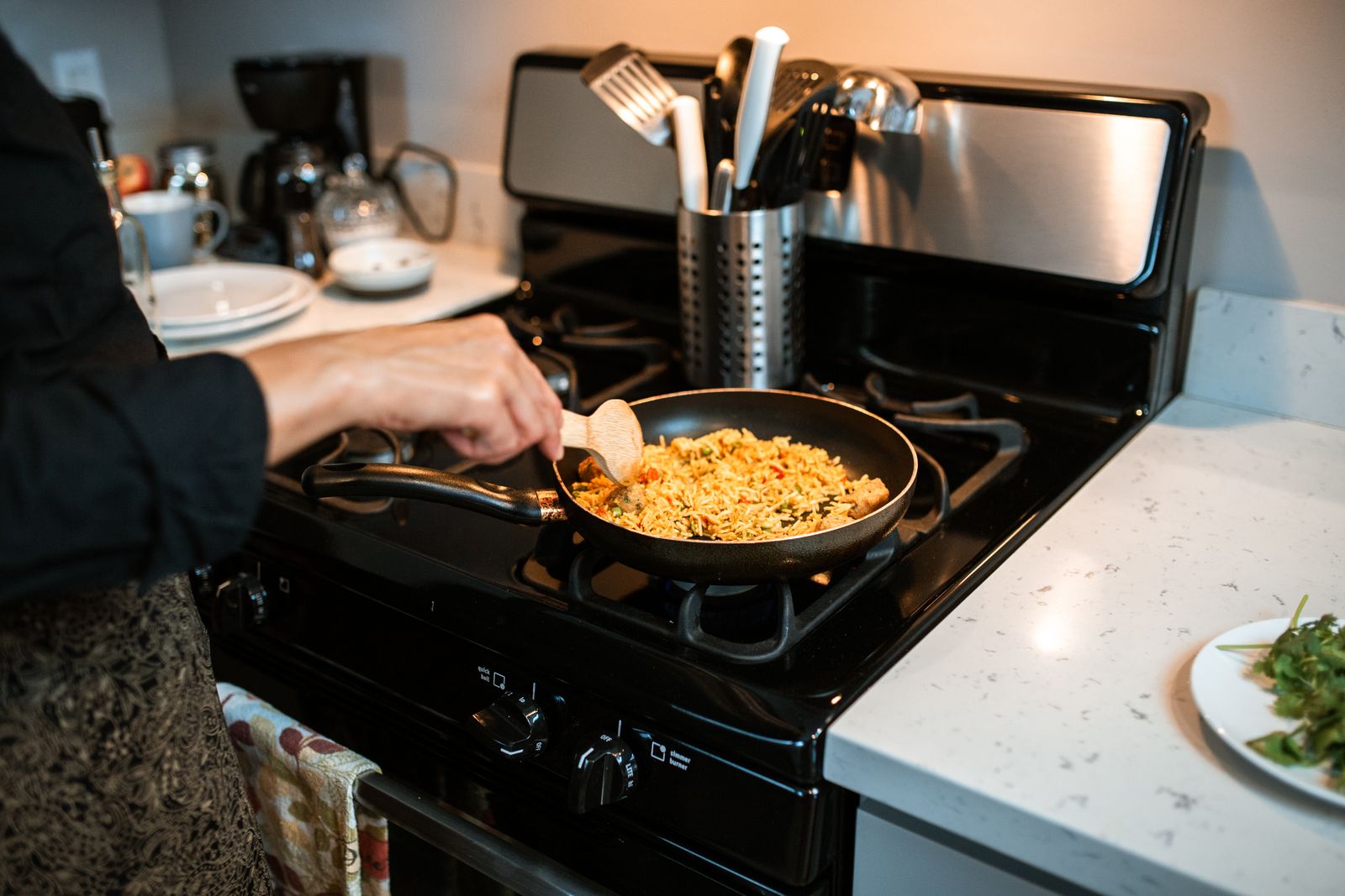 A person cooking rice pilaf using a frying pan on a gas stove in a home kitchen.