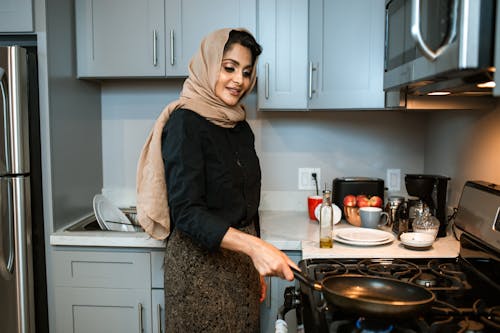 Content Arabic woman with frying pan in modern kitchen