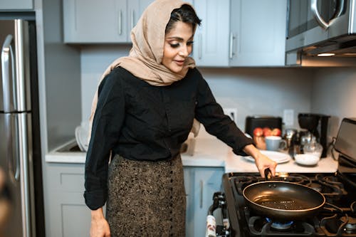 Content Arabic woman standing with frying pan in kitchen
