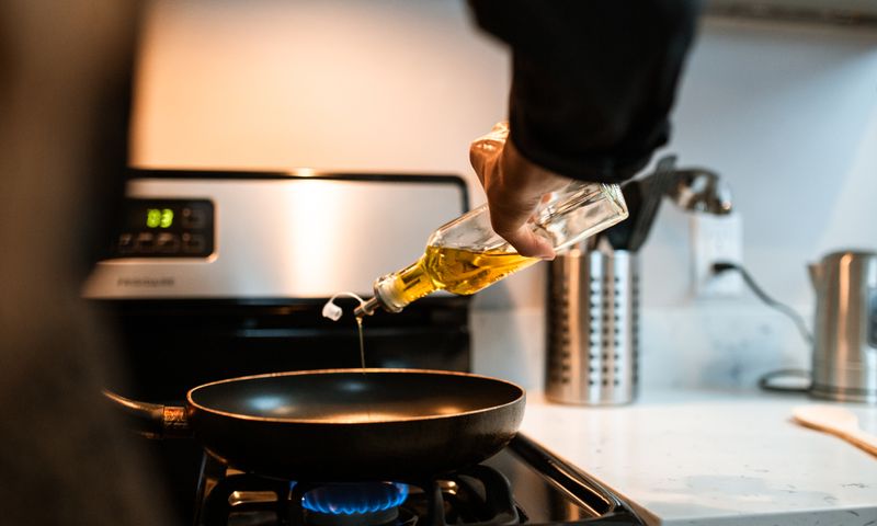 Óleo vegetal sendo vertido em frigideira durante cozimento em cozinha doméstica
