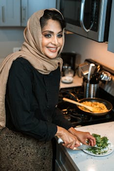 Smiling woman in hijab chopping cilantro in a modern kitchen.