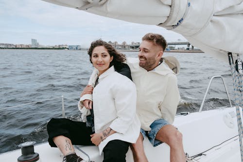 Free Man in White Suit Jacket Sitting Beside Woman in Blue Denim Shorts on Boat Stock Photo