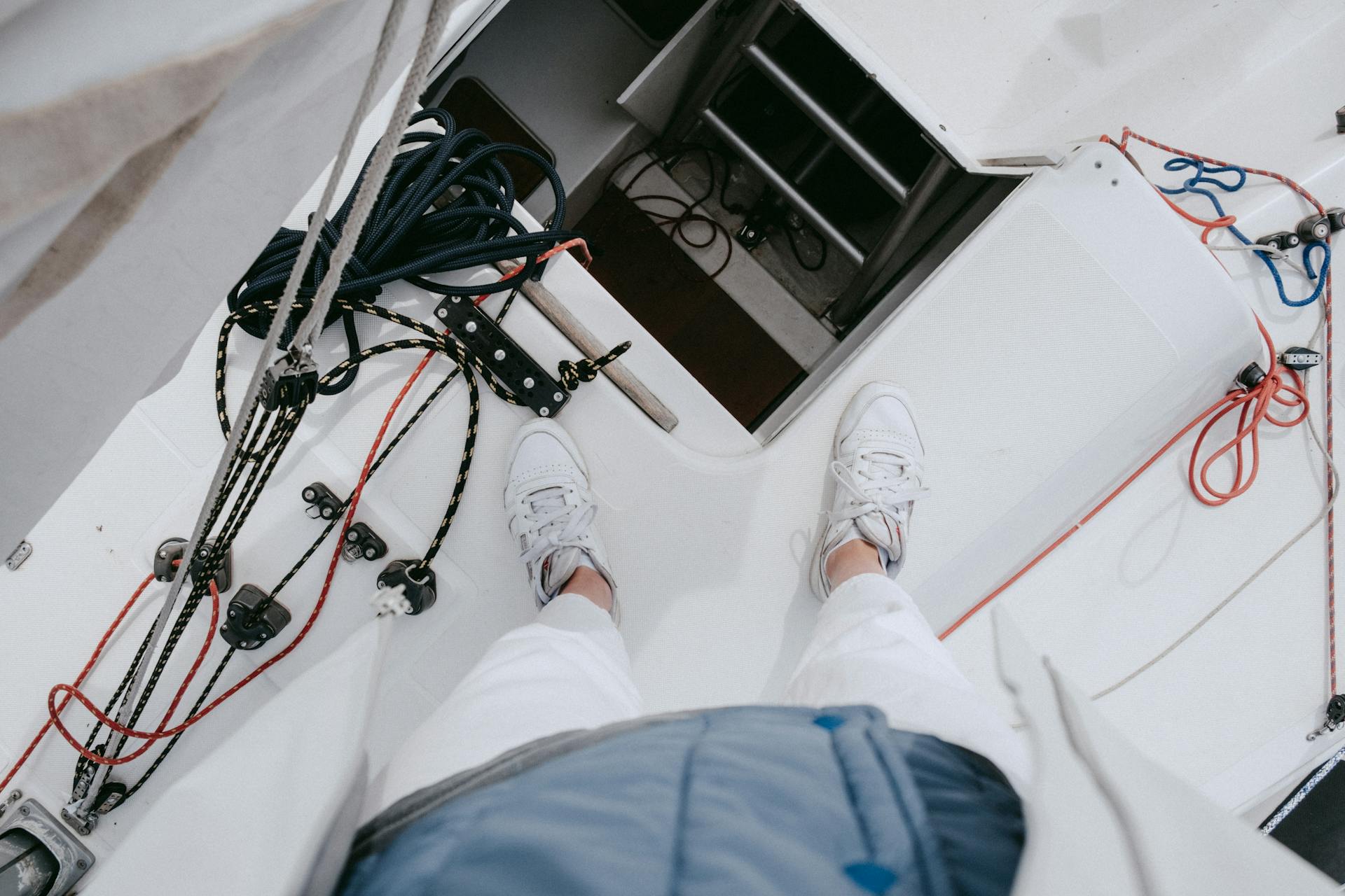 An overhead view of yacht deck showing nautical ropes, rigging, and white sneakers in a summer setting.