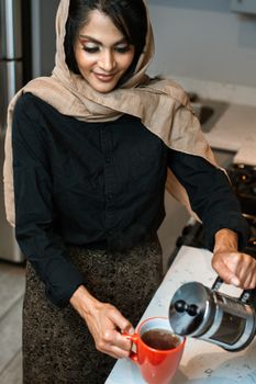 在舒适的厨房里，戴着头巾的穆斯林妇女将法国新闻界的饮料倒入杯中