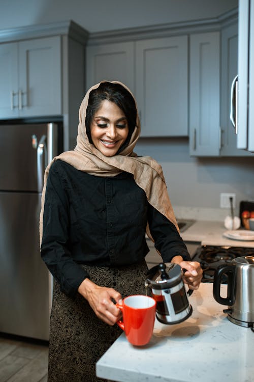 Photo of a Woman Pouring Coffee into a Red Mug