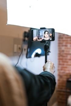Vlogger creating content using a smartphone mounted on a tripod with indoor lighting.