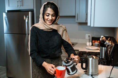 Photo of a Woman with a Brown Hijab Pouring Coffee into a Mug