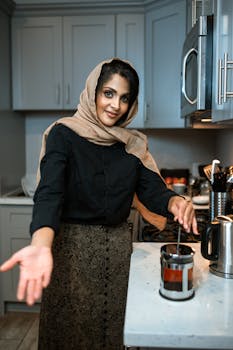 Woman in hijab using French press in a stylish kitchen setting, brewing coffee.