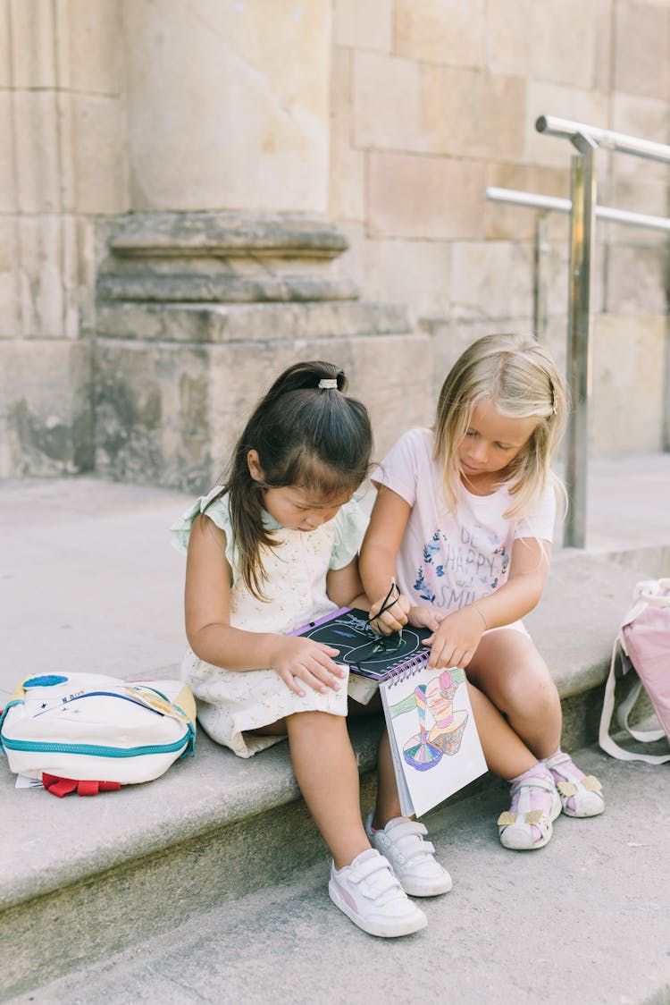 Best Friends Drawing On A Drawing Book While Sitting On The Steps