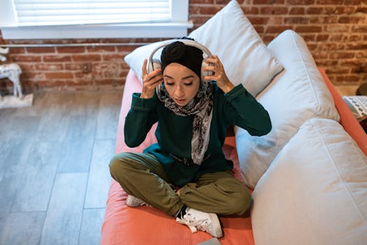 Young woman in casual wear with headphones, sitting on a sofa indoors, enjoying music.
