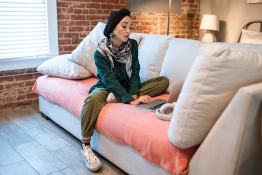 Woman in traditional wear focused on laptop, working remotely from a cozy couch.
